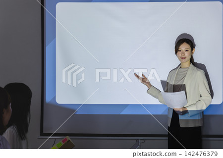A female business person extends her hand to explain from beside the screen. A female business person extends her hand to explain from beside the screen. 142476379