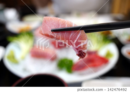 Holding a Thick and Fresh Piece of Premium Tuna Sashimi with Chopsticks Holding a Thick and Fresh Piece of Premium Tuna Sashimi with Chopsticks 142476492