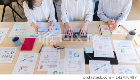 A team working on their tasks with graphs, documents, and IT equipment spread all over their desks. A team working on their tasks with graphs, documents, and IT equipment spread all over their desks. 142476497