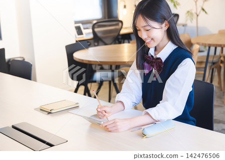 一名高中女生一邊看手機一邊做筆記。 一名高中女生一邊看手機一邊做筆記。 142476506