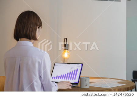 A female employee's back as she checks growth graphs of performance and sales data on her laptop. A female employee's back as she checks growth graphs of performance and sales data on her laptop. 142476520