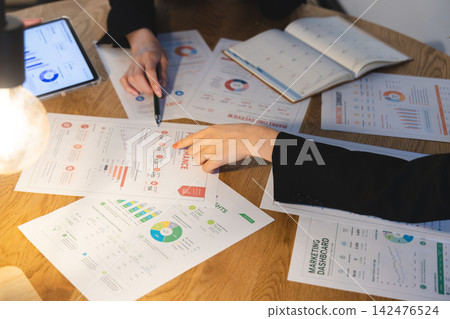 The team discusses the data and documents spread out on the table, pointing to them on tablets. The team discusses the data and documents spread out on the table, pointing to them on tablets. 142476524