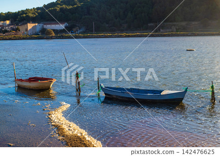 Traditional vintage wooden fishing boats moored in the calm lagoon of Etang de Gruissan with a soft pinkish hue on the water surface in Occitanie, South of France Traditional vintage wooden fishing boats moored in the calm lagoon of Etang de Gruissan with a soft pinkish hue on the water surface in Occitanie, South of France 142476625