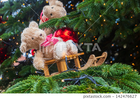Close-up of a Christmas tree branches decorated with a cute teddy bear ornament, red baubles and glowing fairy lights Close-up of a Christmas tree branches decorated with a cute teddy bear ornament, red baubles and glowing fairy lights 142476627