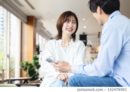一對年輕男女一邊看著智慧型手機螢幕，一邊愉快地交談著。 142476901