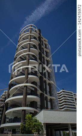 Low angle view of a modern residential building with curved white balconies and a blue sky Low angle view of a modern residential building with curved white balconies and a blue sky 142476972