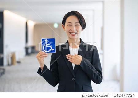 A woman holding a wheelchair symbol. (Keywords: disabled, elderly, barrier-free, caregiving, welfare, safety, security, compassion, support) A woman holding a wheelchair symbol. (Keywords: disabled, elderly, barrier-free, caregiving, welfare, safety, security, compassion, support) 142477724