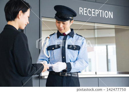 一名女子向保安出示一張卡片。身分證、身分識別卡、員工證、門禁卡、票券、犯罪預防、保全、身分驗證。 一名女子向保安出示一張卡片。身分證、身分識別卡、員工證、門禁卡、票券、犯罪預防、保全、身分驗證。 142477750