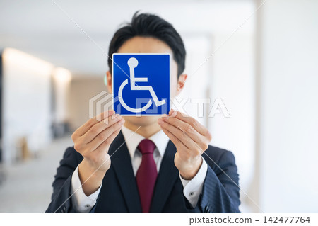 A man holding a wheelchair symbol. (Keywords: disabled, elderly, barrier-free, caregiving, welfare, safety, security, consideration, parking, facility) A man holding a wheelchair symbol. (Keywords: disabled, elderly, barrier-free, caregiving, welfare, safety, security, consideration, parking, facility) 142477764