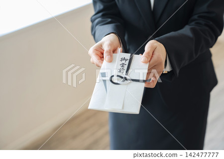 一位女士手捧慰問信封。葬禮、守靈、哀悼者、殯儀館、喪服、追悼會、獻給逝者的祭品、祭品、儀式廳。 一位女士手捧慰問信封。葬禮、守靈、哀悼者、殯儀館、喪服、追悼會、獻給逝者的祭品、祭品、儀式廳。 142477777