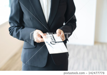 一位女士手捧慰問信封。葬禮、守靈、哀悼者、殯儀館、喪服、追悼會、獻給逝者的祭品、祭品、儀式廳。 一位女士手捧慰問信封。葬禮、守靈、哀悼者、殯儀館、喪服、追悼會、獻給逝者的祭品、祭品、儀式廳。 142477778