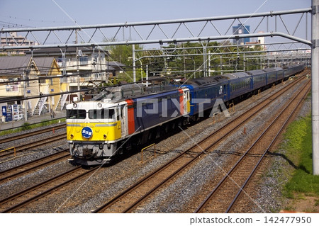 A standard-angle photograph of the "Hokutosei" sleeper express train, pulled by a Cassiopeia-colored EF81 locomotive, traveling along a double-track railway line (Saitama Prefecture). A standard-angle photograph of the "Hokutosei" sleeper express train, pulled by a Cassiopeia-colored EF81 locomotive, traveling along a double-track railway line (Saitama Prefecture). 142477950