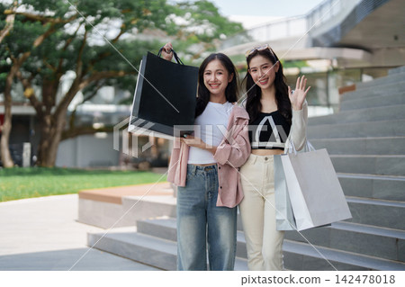 Asian female friends holding shopping bags outside modern retail mall Asian female friends holding shopping bags outside modern retail mall 142478018
