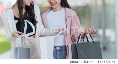 Cropped shot of two women opening paper shopping bag outdoors Cropped shot of two women opening paper shopping bag outdoors 142478075