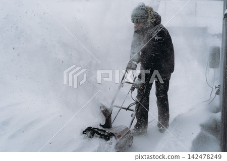 man clearing snowin countryside using electric snow blower man clearing snowin countryside using electric snow blower 142478249