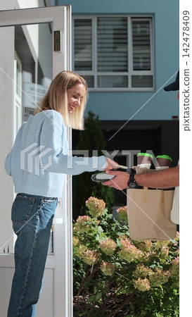 Vertical video. Woman open door to a delivery man on a bike wearing yellow thermal backpack with POS wireless terminal for smartphone paying and recieves coffee and food in paper bag. Food delivery Vertical video. Woman open door to a delivery man on a bike wearing yellow thermal backpack with POS wireless terminal for smartphone paying and recieves coffee and food in paper bag. Food delivery 142478409