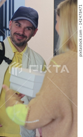 Vertical video. Pizza man courier is delivering an order to a woman customer. View from the apartment. Inside shot. Food delivery concept. Vertical video. Pizza man courier is delivering an order to a woman customer. View from the apartment. Inside shot. Food delivery concept. 142478471