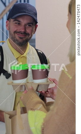 Vertical video. A food delivery person in a yellow uniform. Delivering coffee and food to a person's home. View from the apartment. Inside shot. Food delivery concept. Vertical video. A food delivery person in a yellow uniform. Delivering coffee and food to a person's home. View from the apartment. Inside shot. Food delivery concept. 142478473