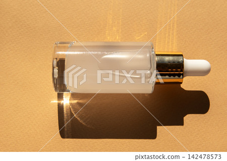 Minimal glass serum bottle with gold dropper casting soft shadow on warm beige background Minimal glass serum bottle with gold dropper casting soft shadow on warm beige background 142478573