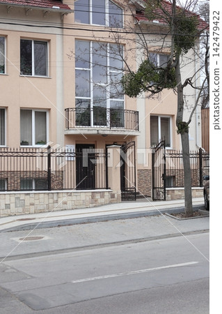 Building with a fence is located on a street in a city on a cloudy day Building with a fence is located on a street in a city on a cloudy day 142479422