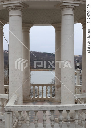 A structure with tall white columns overlooks a body of water. 142479439