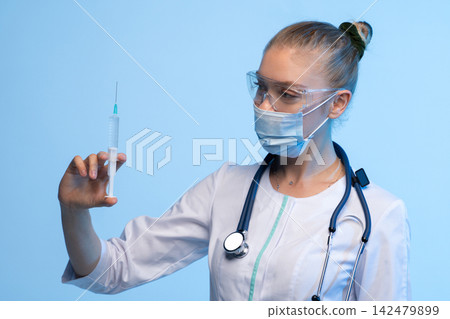 Female doctor wearing medical mask and safety goggles, holding syringe with vaccine, preparing for injection Female doctor wearing medical mask and safety goggles, holding syringe with vaccine, preparing for injection 142479899