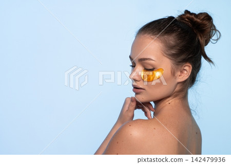 Woman with eye patches enjoying golden hydrogel under eye treatment for skincare, applying beauty product for hydration and wellness Woman with eye patches enjoying golden hydrogel under eye treatment for skincare, applying beauty product for hydration and wellness 142479936