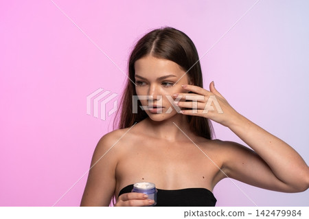 Young woman applying moisturizer on her cheek for a healthy glow and daily beauty skincare routine Young woman applying moisturizer on her cheek for a healthy glow and daily beauty skincare routine 142479984