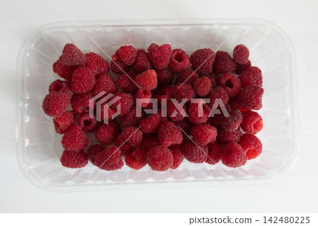Fresh raspberries packed in a transparent plastic food container on a white background. Top view of red ripe berries for food packaging, grocery, retail and healthy eating concepts Fresh raspberries packed in a transparent plastic food container on a white background. Top view of red ripe berries for food packaging, grocery, retail and healthy eating concepts 142480225