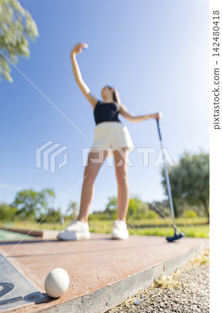 Girl preparing to hit a golf ball on a sunny day at a golf course in the afternoon with blue skies Girl preparing to hit a golf ball on a sunny day at a golf course in the afternoon with blue skies 142480418