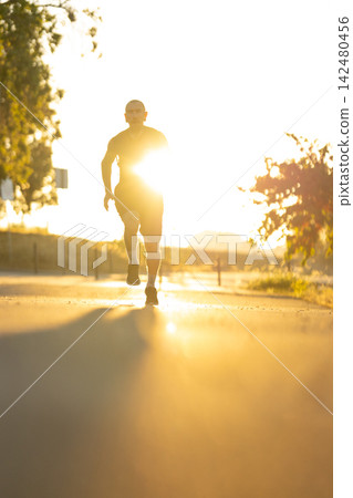 Runner exercises on a path during sunset near trees and open fields Runner exercises on a path during sunset near trees and open fields 142480456