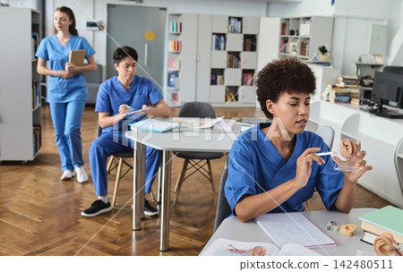 Healthcare intern doctor analyzing outer ear morphology on an acrylic stand with open anatomy manuals in the library Healthcare intern doctor analyzing outer ear morphology on an acrylic stand with open anatomy manuals in the library 142480511