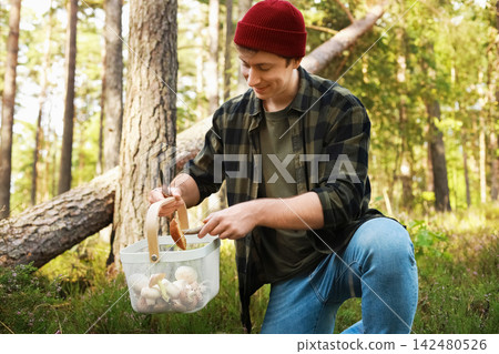man enjoys the autumn outdoors, foraging and harvesting a wild mushroom in the forest. He connects with nature while adding to his full basket. man enjoys the autumn outdoors, foraging and harvesting a wild mushroom in the forest. He connects with nature while adding to his full basket. 142480526