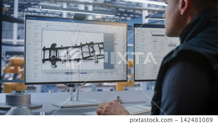 Male Operator Managing Automated Production Workflows and CAD Blueprints on Dual Screens 142481089