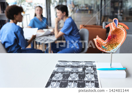 Sectional stomach replica illustrating mucosal inflammation and computed tomography sheets with interns conferring at a study table Sectional stomach replica illustrating mucosal inflammation and computed tomography sheets with interns conferring at a study table 142481144