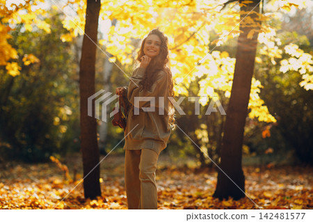 Smiling young woman walking in autumn forest with the yellow leaves at sunset. Smiling young woman walking in autumn forest with the yellow leaves at sunset. 142481577