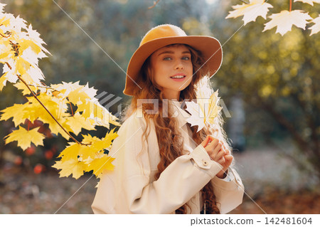 Smiling young woman portrait in the autumn forest with the yellow leaves at sunset. 142481604