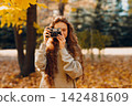 Smiling young woman with the photo camera shooting the forest trees with the yellow leaves at sunset. 142481609