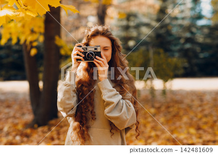 Smiling young woman with the photo camera shooting the forest trees with the yellow leaves at sunset. Smiling young woman with the photo camera shooting the forest trees with the yellow leaves at sunset. 142481609
