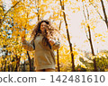 Smiling young woman plays and jumping dancing in the autumn forest with the yellow leaves at sunset. 142481610