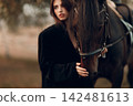 Young woman in black with her horse at sunset outdoors. 142481613