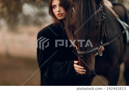 Young woman in black with her horse at sunset outdoors. Young woman in black with her horse at sunset outdoors. 142481613