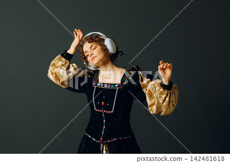 Portrait of a young aristocratic woman with headphones on her head and dressed in a medieval dress listens classical music. Portrait of a young aristocratic woman with headphones on her head and dressed in a medieval dress listens classical music. 142481618