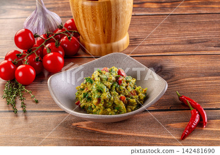 Fresh homemade guacamole in bowl with ingredients on rustic wooden table Fresh homemade guacamole in bowl with ingredients on rustic wooden table 142481690