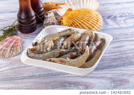 Raw shrimp in white bowl with seashells and spices on rustic wooden table Raw shrimp in white bowl with seashells and spices on rustic wooden table 142481692