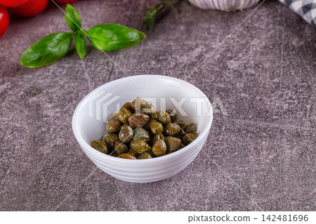Pickled capers in white bowl on stone table with fresh basil and tomatoes 142481696