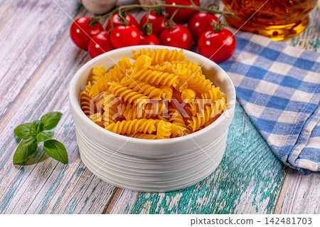Uncooked fusilli pasta in bowl with fresh cherry tomatoes and basil on rustic wooden table Uncooked fusilli pasta in bowl with fresh cherry tomatoes and basil on rustic wooden table 142481703