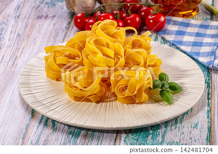 Raw tagliatelle pasta nests on plate with fresh cherry tomatoes and basil 142481704