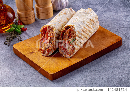 Grilled shawarma wraps with meat and vegetables on wooden cutting board Grilled shawarma wraps with meat and vegetables on wooden cutting board 142481714