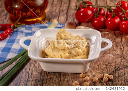 Creamy hummus dip in white bowl, fresh chickpeas, red cherry tomatoes, chili peppers, garlic, green onions, wooden background Creamy hummus dip in white bowl, fresh chickpeas, red cherry tomatoes, chili peppers, garlic, green onions, wooden background 142481912